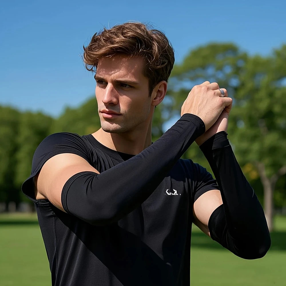 Man wearing a black long-sleeve athletic shirt with a brand logo, standing outdoors with trees and blue sky in the background.